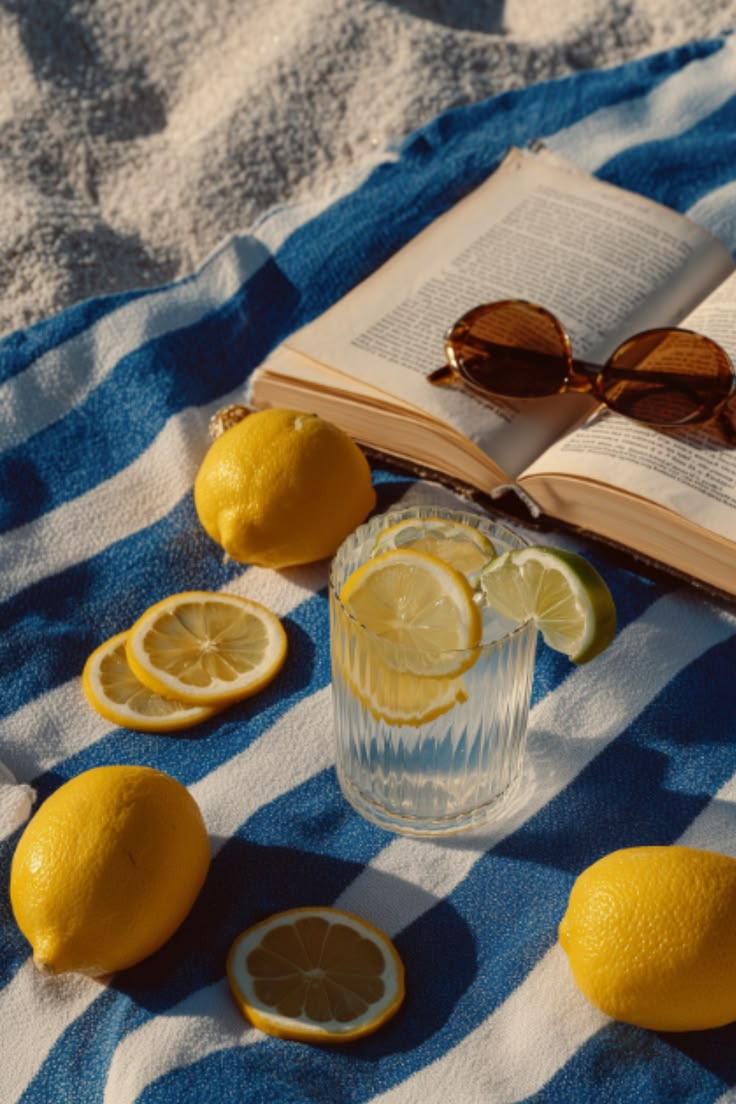 Open book, citrus drink and sunglasses on a striped beach towel